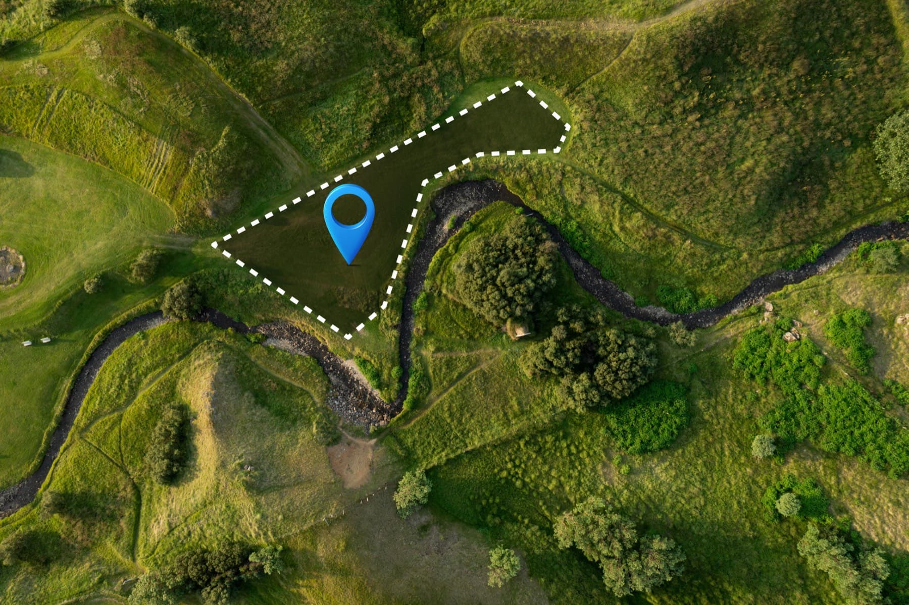 Aerial view of a land plot with its boundary marked as a dashed line and a location pin at the centre